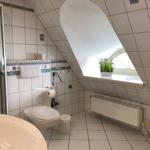 Badezimmer mit Dusche, Toilette und Fenster unter Dachschrägen.