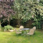 Garten mit runden Tisch und vier Stühlen unter Bäumen.