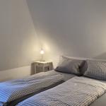 Doppelbett mit kariertem Bettwäsche und Nachttisch mit Lampe unter schräger Decke.