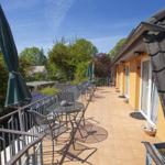 Terrasse mit Tischen, Stühlen und grünen Sonnenschirmen. Gelb gestrichene Fassade und Dachziegel.
