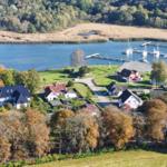 Häuser am Ufer mit Bootsharbor und Wald im Hintergrund.