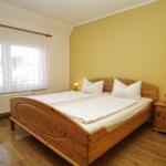 Ein Schlafzimmer mit Holzbett, Nachttisch und Fenster mit Vorhängen.