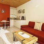 Wohn- und Küchenbereich mit rotem Sofa, Holztisch und weißen Schränken.