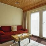 Ein Wohnzimmer mit rotem Sofa, Holztisch und Fenster zur Terrasse.