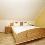 Schlafzimmer mit Holzbett, Nachttischen und Lampen unter schrägem Dach.