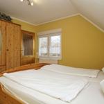 Schlafzimmer mit Holzbett, Kleiderschrank und Fenster.