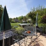 Terrasse mit Tisch, Stühlen und grünen Sonnenschirmen. Blick auf Garten und Bäume.