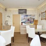 Essbereich mit zwei Tischen, weißen Stühlen und Wandbildern. Holzfußboden und vertikale Wandverkleidung.