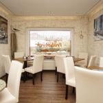 Esszimmer mit Holztischen, weißen Stühlen und maritimen Wandbildern.