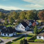Dorf mit Häusern, Grünflächen und Wald im Hintergrund.