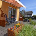 Terrasse mit Sitzgelegenheiten und Blumenbeeten vor einem gelben Haus.
