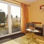 Zimmer mit zwei Sesseln, Tisch und Blick auf Balkon mit Pflanzen.