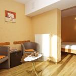 Zimmer mit Schlafbereich, zwei Sesseln, Tisch und Kühlschrank.