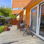 Terrasse mit Sitzgruppe unter orangefarbenem Markisenüberdachung. Holzdecke und Garten im Hintergrund.