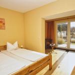 Schlafzimmer mit Doppelbett, Holzboden und Balkon mit Gartenblick.