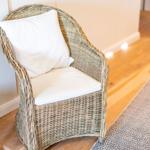 Ein geflochtenes Sitzmöbel mit weißer Polsterung steht auf Holzboden.