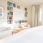 Schlafzimmer mit Bücherregal, Sitzgelegenheiten und Fenster zum Garten.