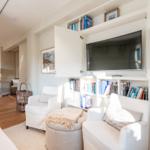 Wohnbereich mit Bücherregalen, TV und weißen Sesseln.