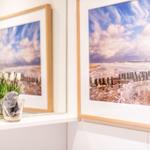 Zwei gerahmte Strandbilder hängen an der Wand. Davor steht eine Vase mit Tulpen und Muscheln.