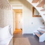 Wohnbereich mit Rattan-Sessel, Treppe und Spiegel an der Wand.