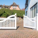 Weißer Torbogen führt zu einem gepflasterten Weg vor einem Haus mit Schilfrohr-Dach.