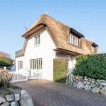 Wohnhaus mit Strohdach, weißen Wänden und gepflastertem Hof.