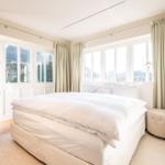 Schlafzimmer mit weißem Bett, großen Fenstern und Holzboden.