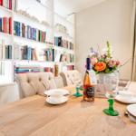 Esstisch mit Stühlen, Bücherregal und Blumenvase.