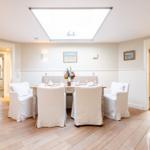 Esszimmer mit Tisch, Stühlen und Deckenfenster. Holzboden und Wandbilder sichtbar.