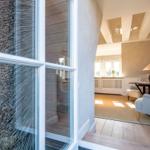 Durch einen Flur mit Holzboden und weißen Wänden gelangt man in ein Wohnzimmer mit Sitzgelegenheiten.