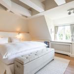 Schlafzimmer mit weißem Bett, Holzboden und großem Fenster.