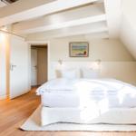 Schlafzimmer mit Dachschräge, weißem Bett und Holzboden.