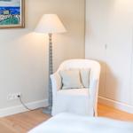 Ein weißer Sessel mit Kissen steht neben einer Stehlampe und einem Schrank.