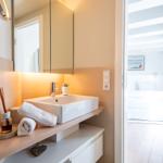 Badezimmer mit Waschbecken und Blick in Schlafzimmer mit Dachschrägen.