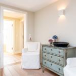 Ein Raum mit zwei weißen Sesseln, einem blauen Schrank und einer Wandlampe.