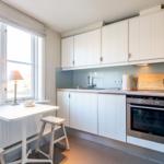 Küche mit weißen Schränken, Edelstahlherd und kleinem Tisch mit Hocker.