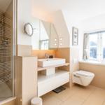 Badezimmer mit Dusche, Waschbecken und Toilette. Fenster mit Vorhängen.