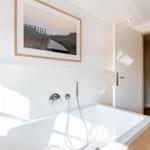 Badezimmer mit Whirlpool, Wandbild und Holzboden im Flur.