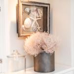 Wandbild mit Meereskunst, Vase mit Trockenpflanze und Glasbehälter auf weißem Regal.