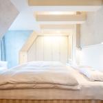 Schlafzimmer mit Doppelbett, weißen Wänden und Holzboden. Dachschräge und integrierte Schränke.