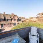 Terrasse mit Tisch, Stuhl und Glas Wein. Blick auf strohgedeckte Häuser und Grünflächen.