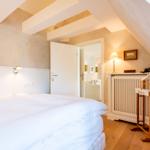 Schlafzimmer mit Dachschräge, Bett, Kleiderständer und Tür zum Wohnbereich.