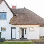 Wohnhaus mit Strohdach, weißen Wänden und zwei Eingängen. Vorgarten mit Pflanzen.