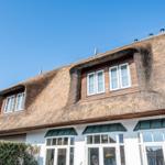 Haus mit Strohdach und weißen Fenstern unter blauem Himmel