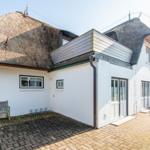 Wohnhaus mit Strohdach, weißer Fassade und Steinpflasterhof.