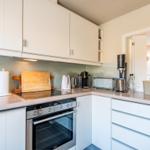 Moderne Küche mit weißen Schränken, Edelstahlherd und Arbeitsplatte.