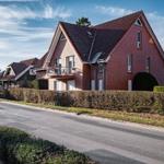Rotes Backsteingebäude mit Balkon und Dachgauben an ruhiger Straße.