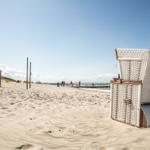 Strand mit weißen Strandkörben und Menschen in der Ferne.