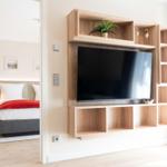 Wohnbereich mit TV-Möbel und Blick in Schlafzimmer mit Bett und Nachttisch.