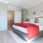 Schlafzimmer mit Doppelbett, Kleiderschrank und Blick in die Badewanne.